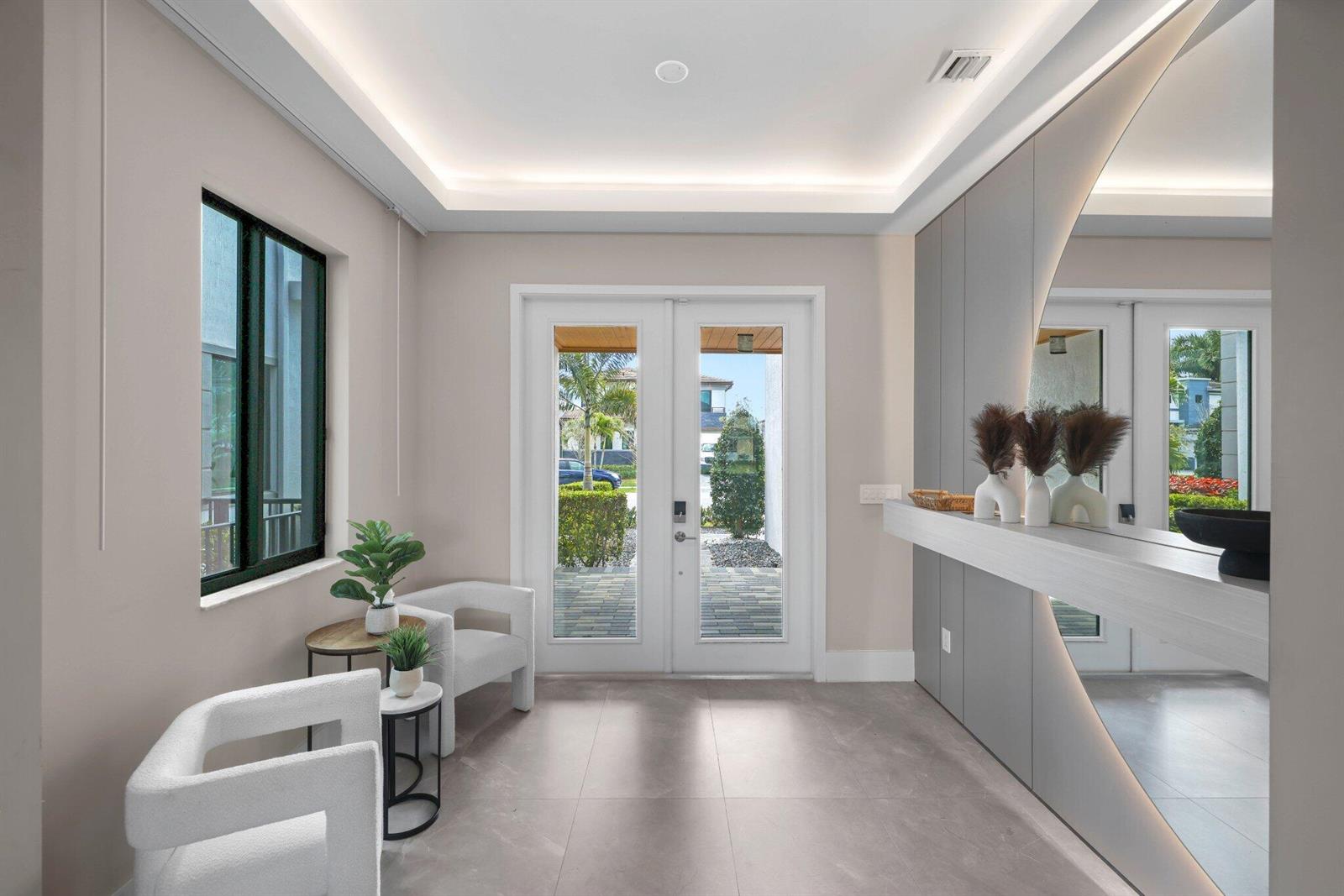 A modern entryway features light gray tile floors, white armchairs, and a large circular mirror — 10725 Passage Way, Parkland FL 33076, PARKLAND, FL