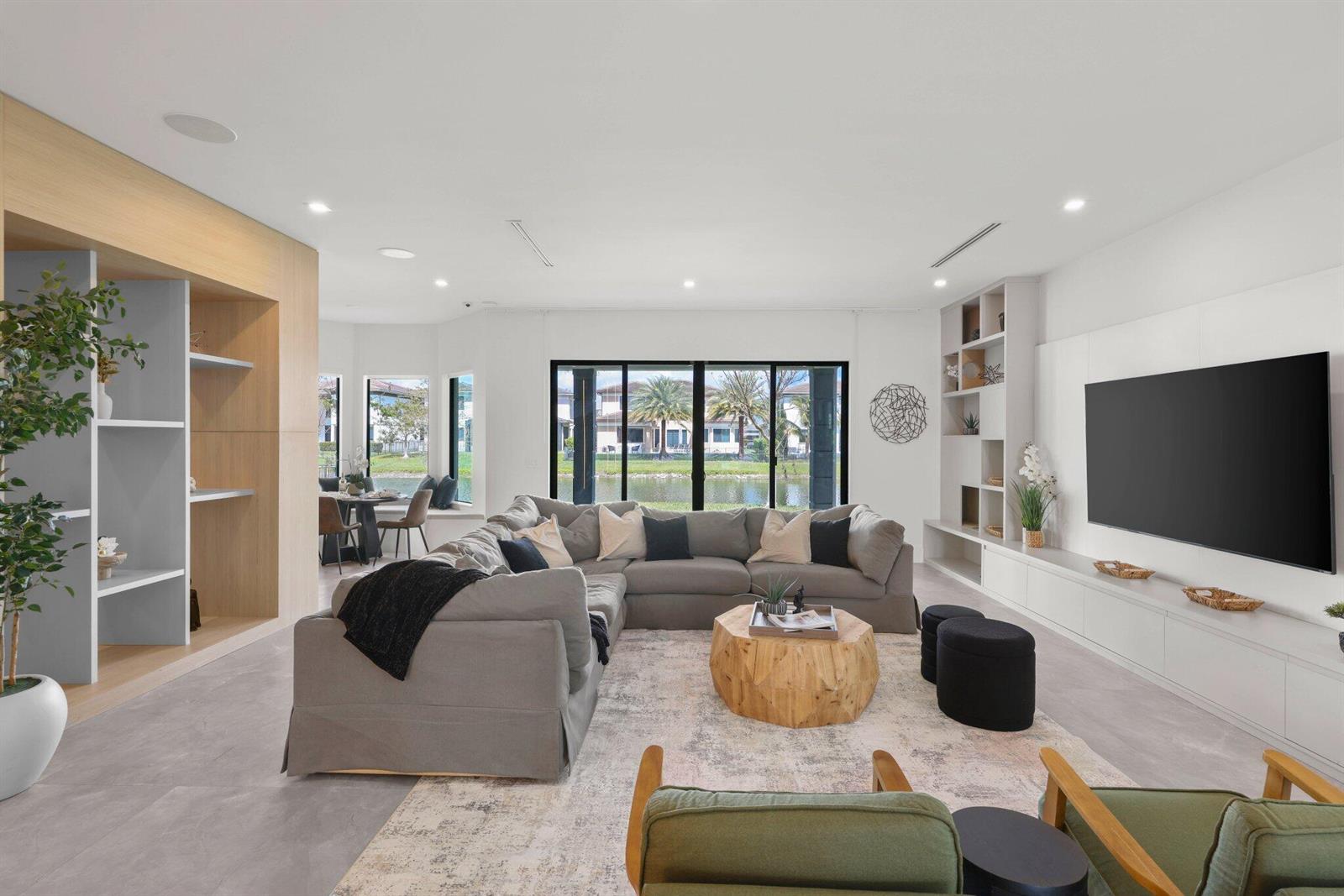 A modern living room features a large grey sectional, wooden coffee table, and waterfront views — 10725 Passage Way, Parkland FL 33076, PARKLAND, FL