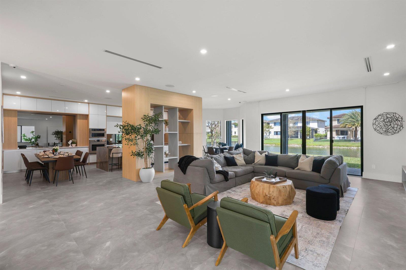 An open-concept living and dining area features gray tile floors, a sectional sofa, and lake views — 10725 Passage Way, Parkland FL 33076, PARKLAND, FL