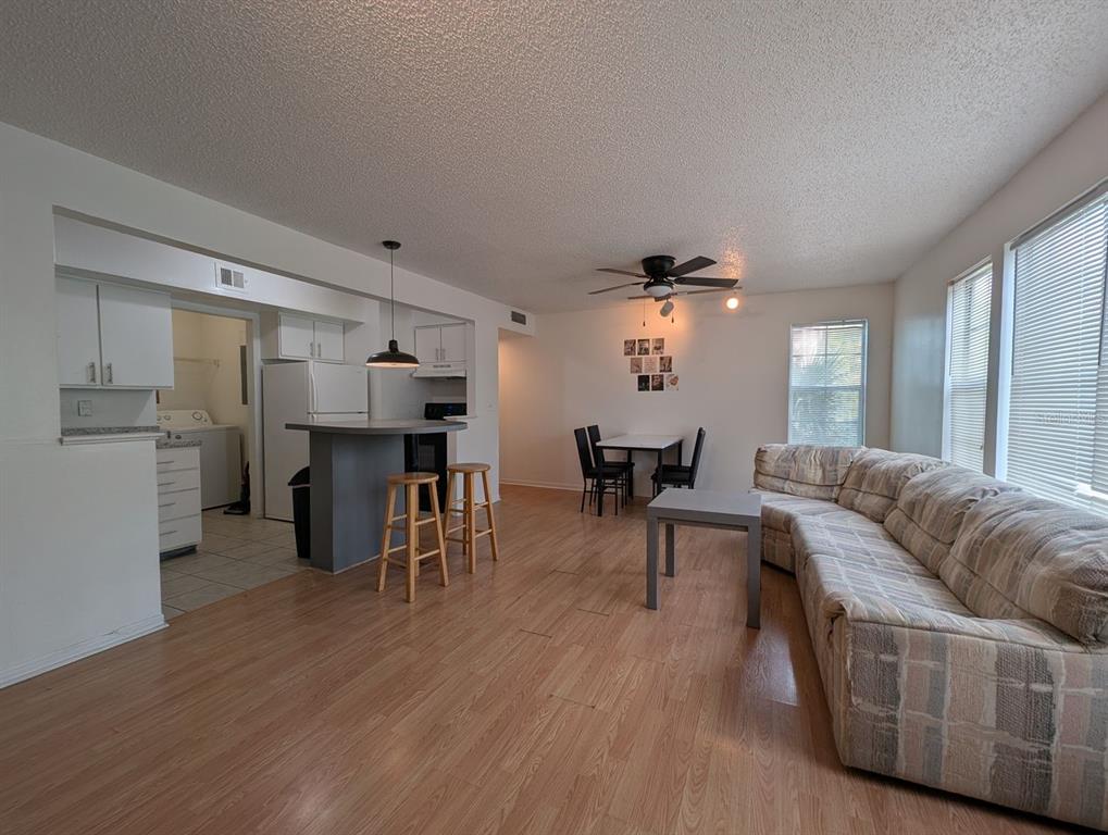An open-concept living and dining area features light wood flooring, a kitchen island, and furniture — 2601 SW ARCHER ROAD UNIT 203, GAINESVILLE, FL