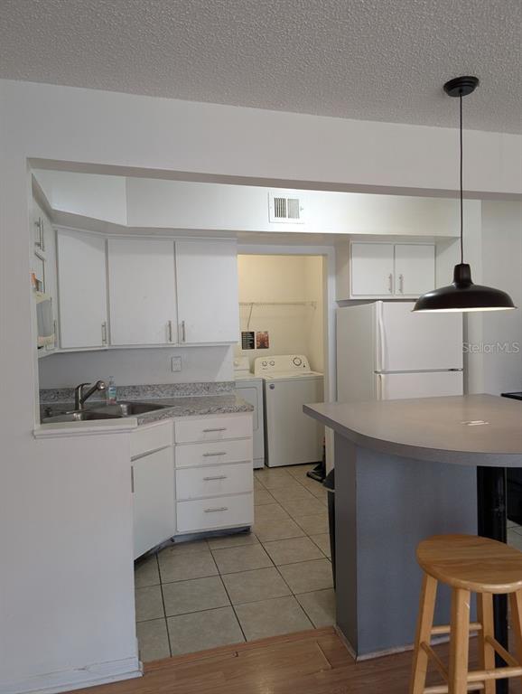 A kitchen with white cabinets, a breakfast bar, and an adjacent laundry room with appliances — 2601 SW ARCHER ROAD UNIT 203, GAINESVILLE, FL