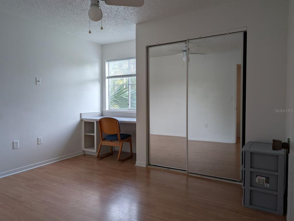 A bedroom with wood-look flooring, a built-in desk, and mirrored sliding closet doors — 2601 SW ARCHER ROAD UNIT 203, GAINESVILLE, FL
