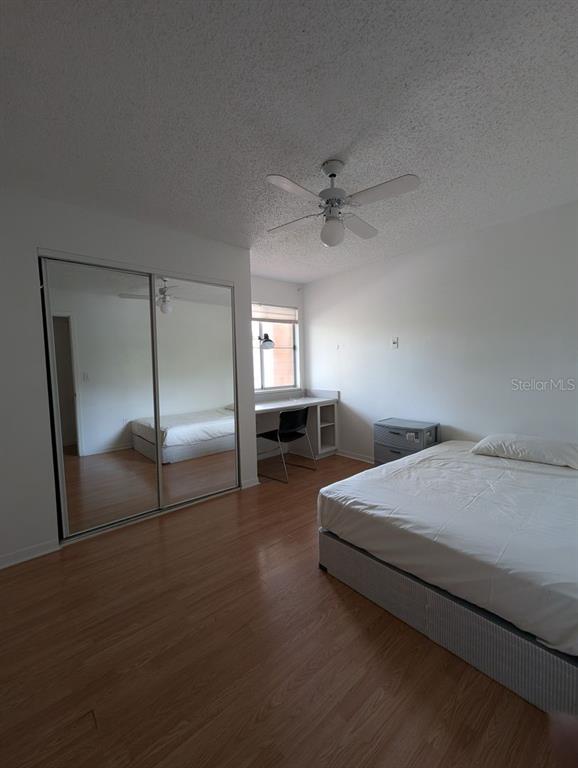 A bedroom with wood-look flooring, a mirrored closet, a built-in desk, and a ceiling fan — 2601 SW ARCHER ROAD UNIT 203, GAINESVILLE, FL