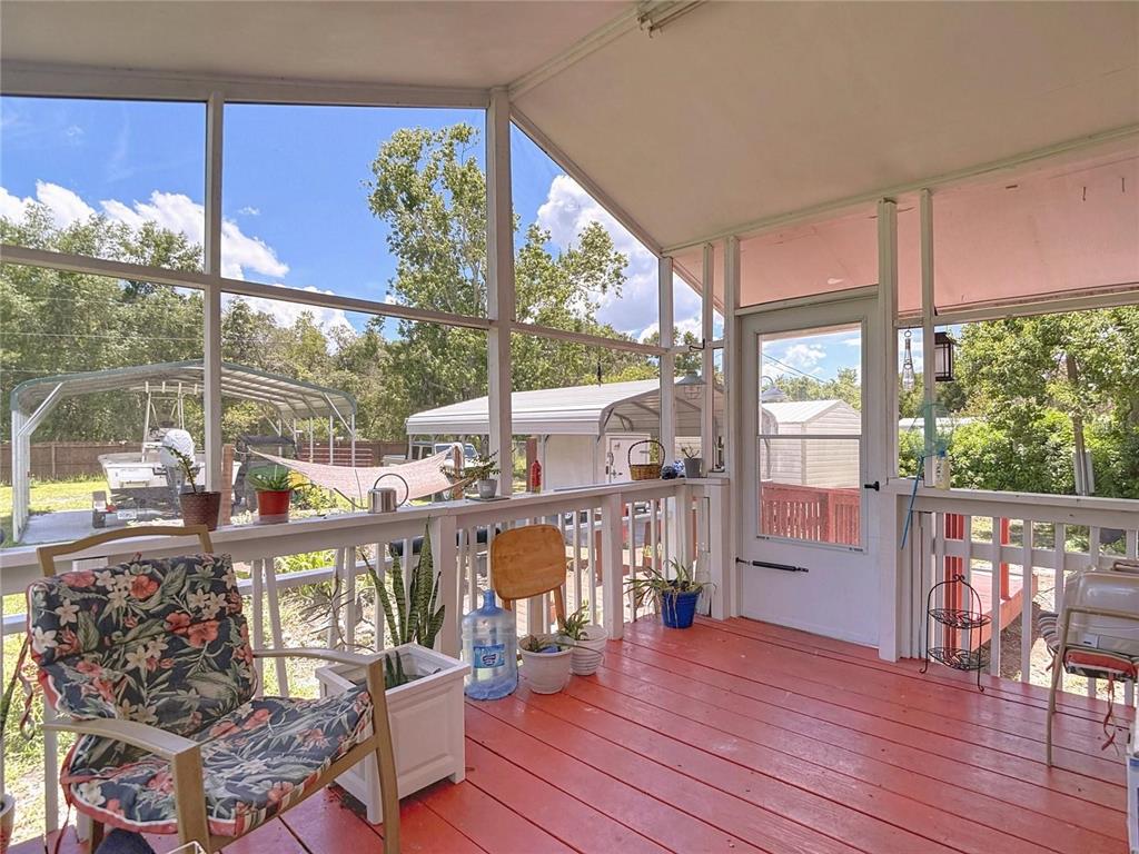 A screened-in porch features a red wooden floor, white railings, and a view of a yard — 9801 UPLAND DRIVE, HUDSON, FL