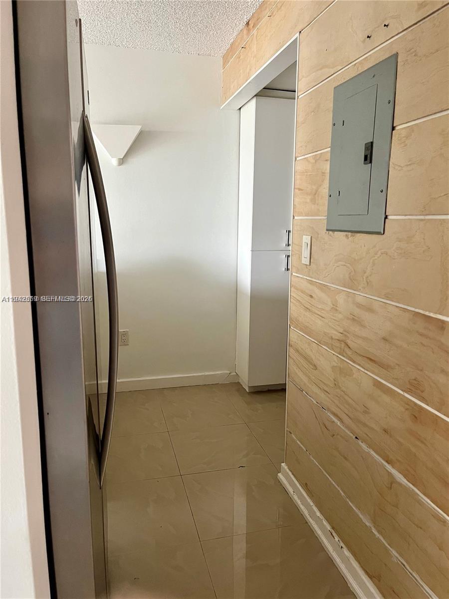 A hallway features light-colored tile flooring, a wood-paneled wall, and a gray electrical panel — 1650 NE 115th St # 507, Miami FL 33181, MIAMI, FL