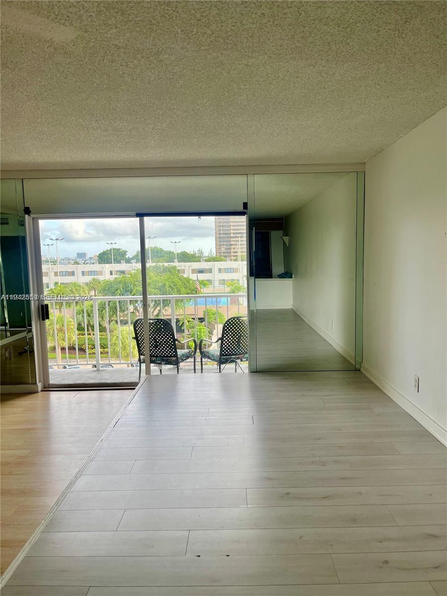 A room with light wood-look flooring features a sliding glass door leading to a balcony — 1650 NE 115th St # 507, Miami FL 33181, MIAMI, FL