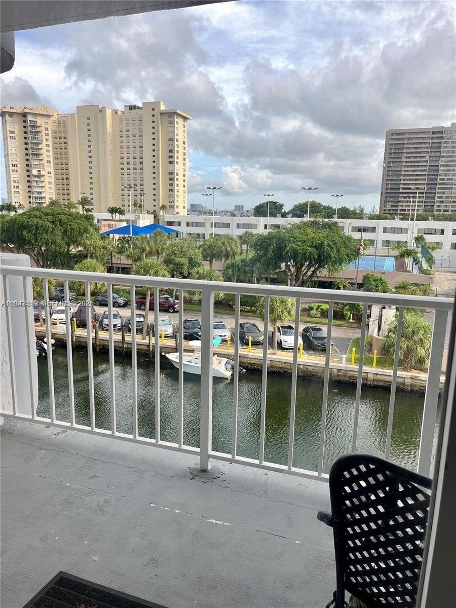 A balcony overlooks a canal, parked cars, and high-rise buildings under a cloudy sky — 1650 NE 115th St # 507, Miami FL 33181, MIAMI, FL