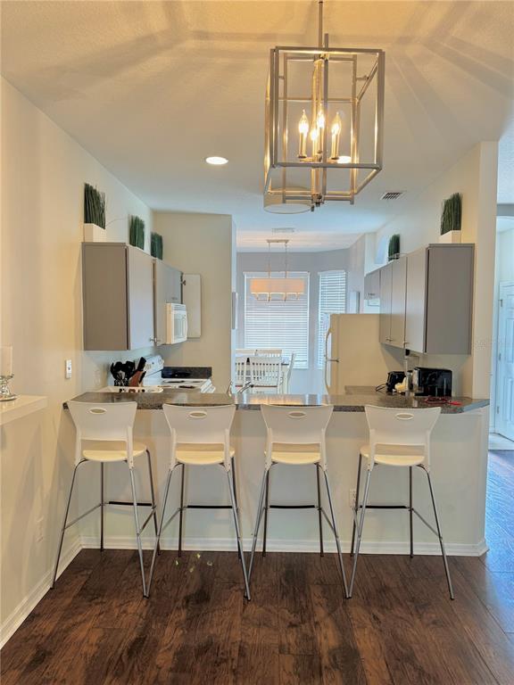 A kitchen features a breakfast bar with four white stools and a large metal pendant light — 1150 S BEACH CIRCLE, KISSIMMEE, FL