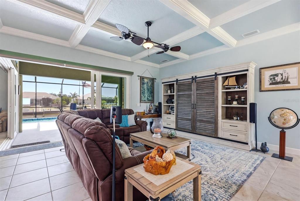 A living room features a coffered ceiling, brown sectional sofa, and sliding doors to a pool — 15610 SEAFOAM CIRCLE, PORT CHARLOTTE, FL