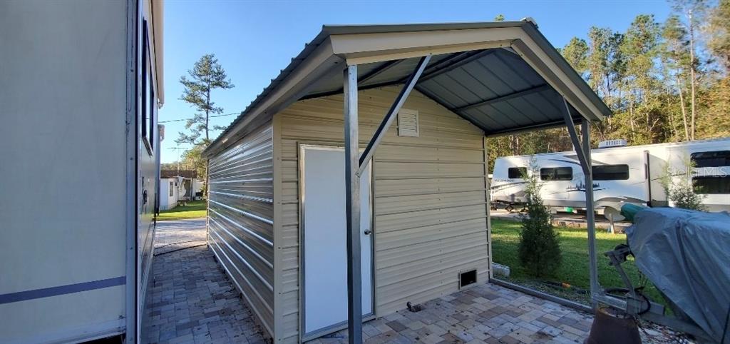 A metal storage shed with an attached carport sits on a paved patio area — 2092 CULBREATH ROAD UNIT A78, BROOKSVILLE, FL