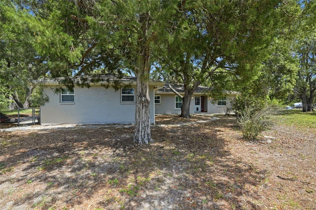 A single-story house with a light-colored exterior sits among large trees on a grassy lot — 15620 HAYS ROAD, SPRING HILL, FL