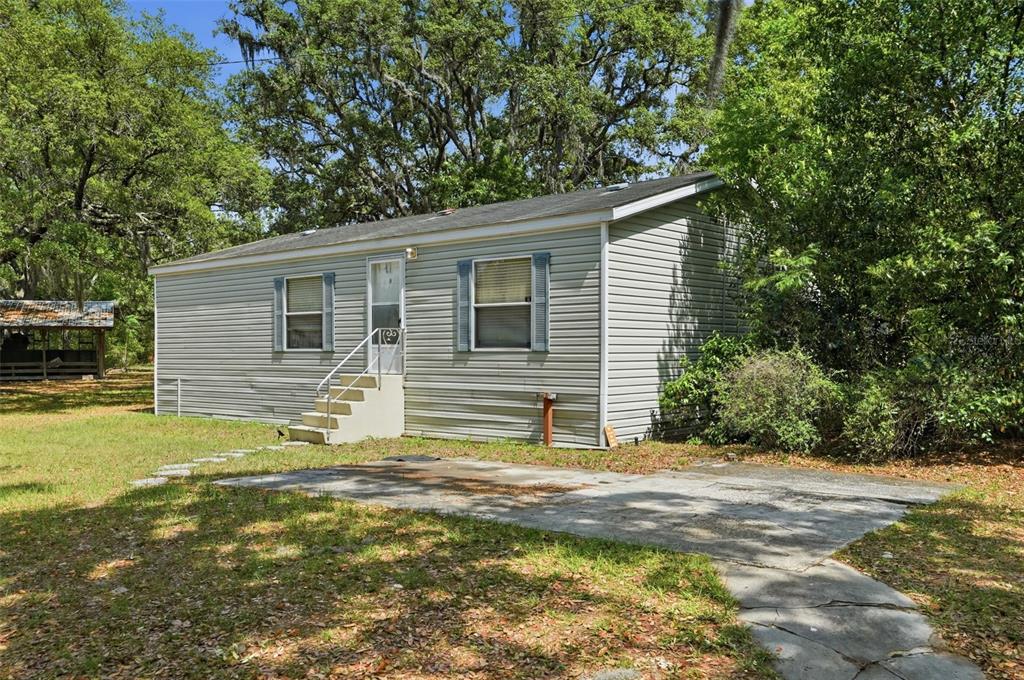 A single-story house with light gray siding sits on a grassy lot with trees — 15620 HAYS ROAD, SPRING HILL, FL
