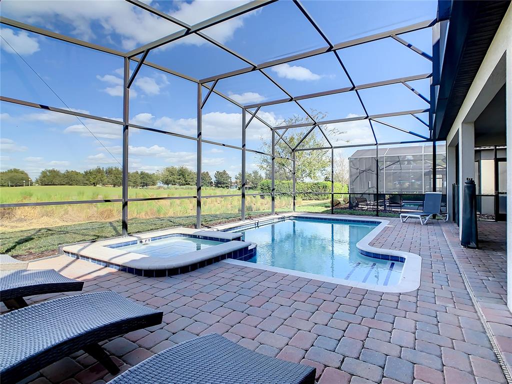 A screened-in pool and hot tub area with a brick paver patio overlooking a field — 9155 CADDIE WAY, DAVENPORT, FL