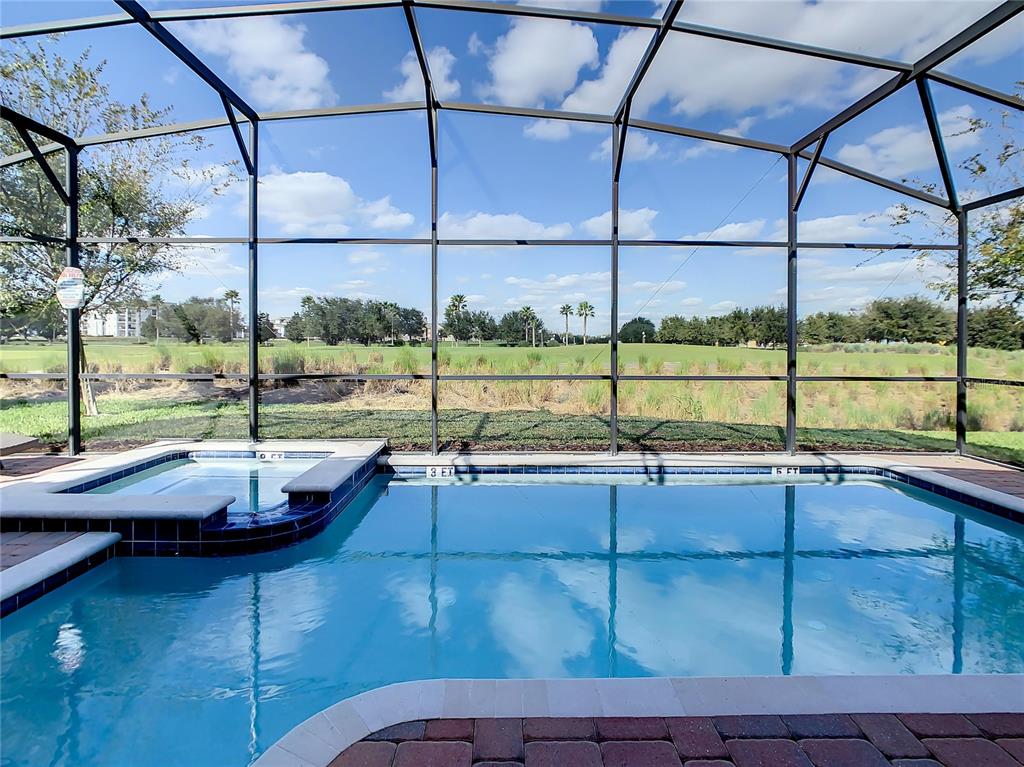 A screened-in swimming pool and spa overlook a grassy field under a blue sky — 9155 CADDIE WAY, DAVENPORT, FL