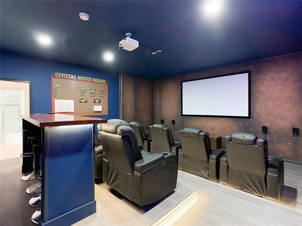 A home theater room features a projector screen, tiered leather seating, and a bar area — 9155 CADDIE WAY, DAVENPORT, FL