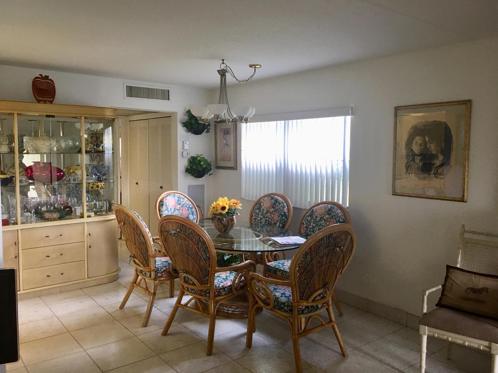 A dining room features a glass-topped table with wicker chairs, a china cabinet, and tile flooring — 99 Saxony C, Delray Beach FL 33446, DELRAY BEACH, FL