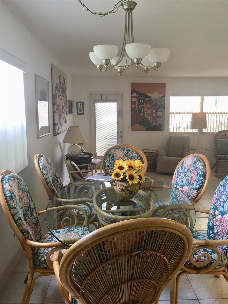 A dining room features a glass-topped rattan table with floral chairs and a chandelier — 99 Saxony C, Delray Beach FL 33446, DELRAY BEACH, FL