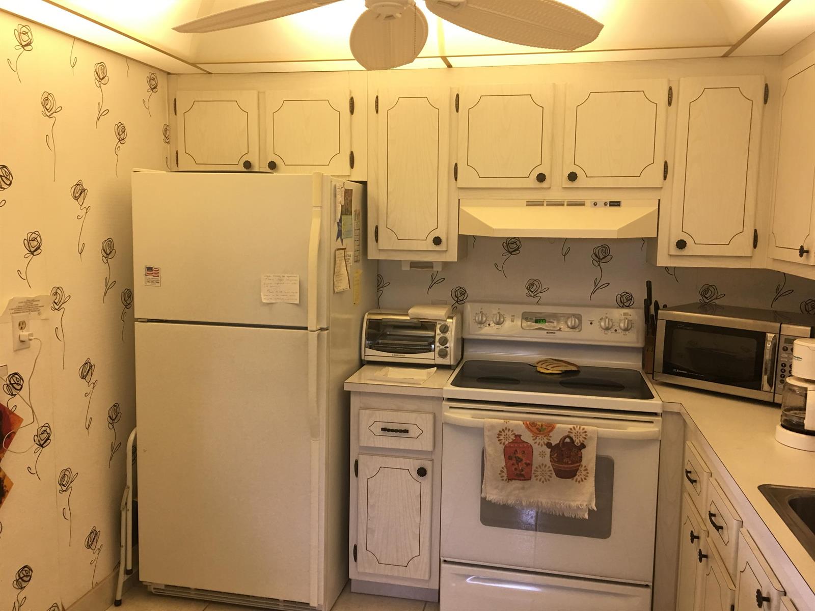 A kitchen with white appliances, white cabinets, and wallpaper featuring a black rose pattern — 99 Saxony C, Delray Beach FL 33446, DELRAY BEACH, FL
