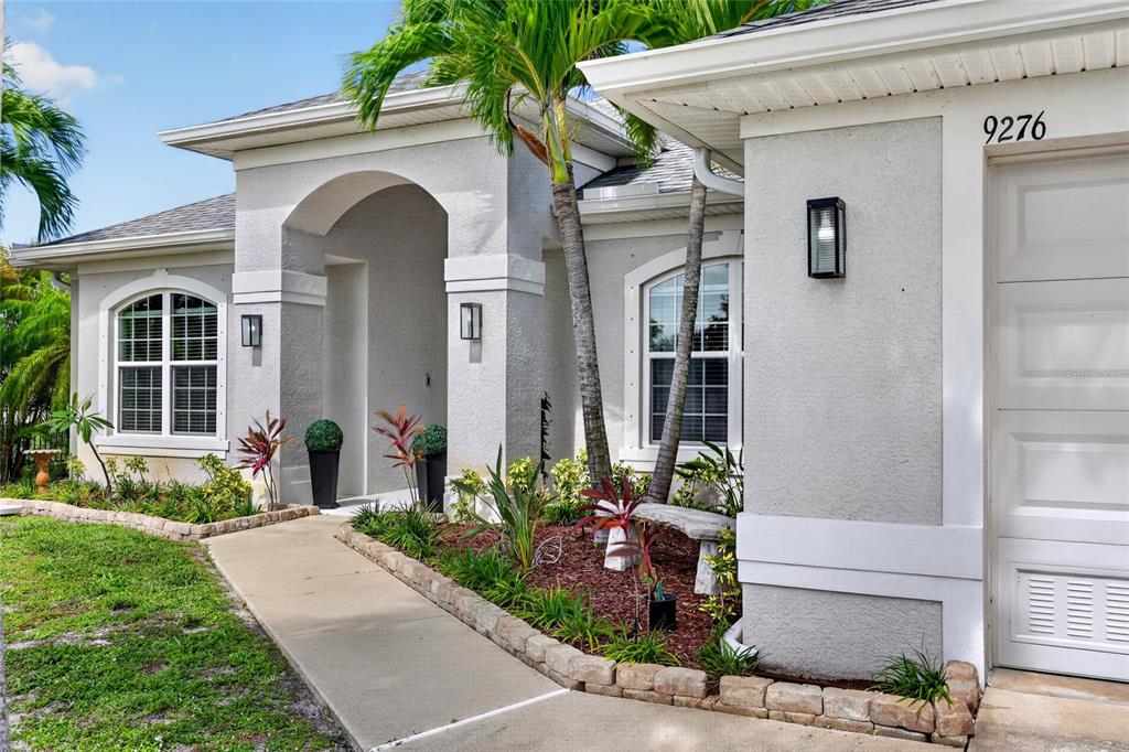 A concrete walkway leads to the arched entryway of a light-colored stucco house — 9276 MIAMI CIRCLE, PORT CHARLOTTE, FL