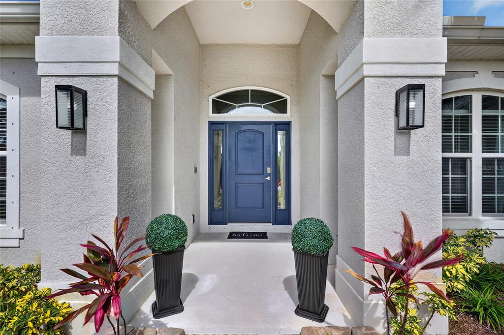 A blue front door with sidelights and a transom window sits under a covered entryway — 9276 MIAMI CIRCLE, PORT CHARLOTTE, FL