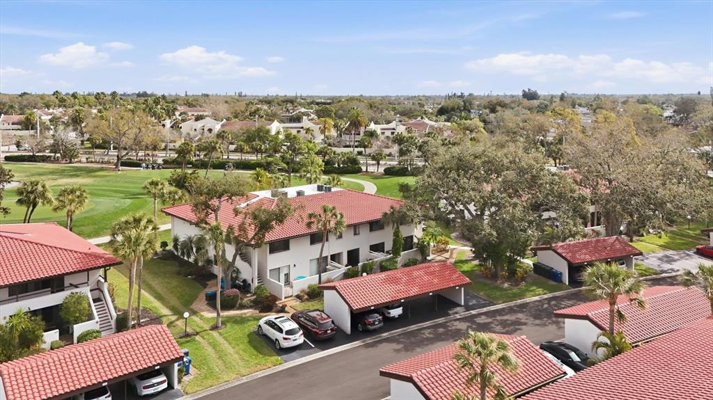 An aerial view shows multi-story apartment buildings with red tile roofs and covered parking spaces — 3500 EL CONQUISTADOR PARKWAY UNIT 144, BRADENTON, FL