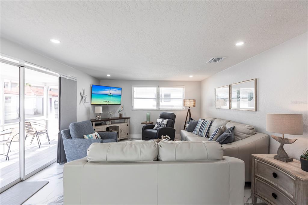 A living room features light-colored furniture, a television, and a sliding glass door to a patio — 6154 MIDNIGHT PASS ROAD UNIT C16, SARASOTA, FL
