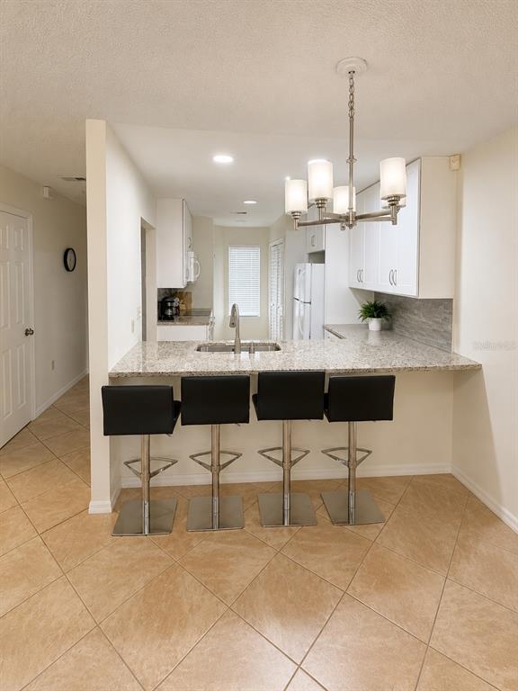 A kitchen features a granite breakfast bar with four black stools and white cabinetry — 5322 11TH STREET CIRCLE E UNIT 5322, BRADENTON, FL