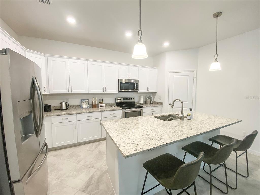 A kitchen features white cabinets, granite countertops, a center island with stools, and stainless appliances — 15936 HONEYSUCKLE STREET, PORT CHARLOTTE, FL