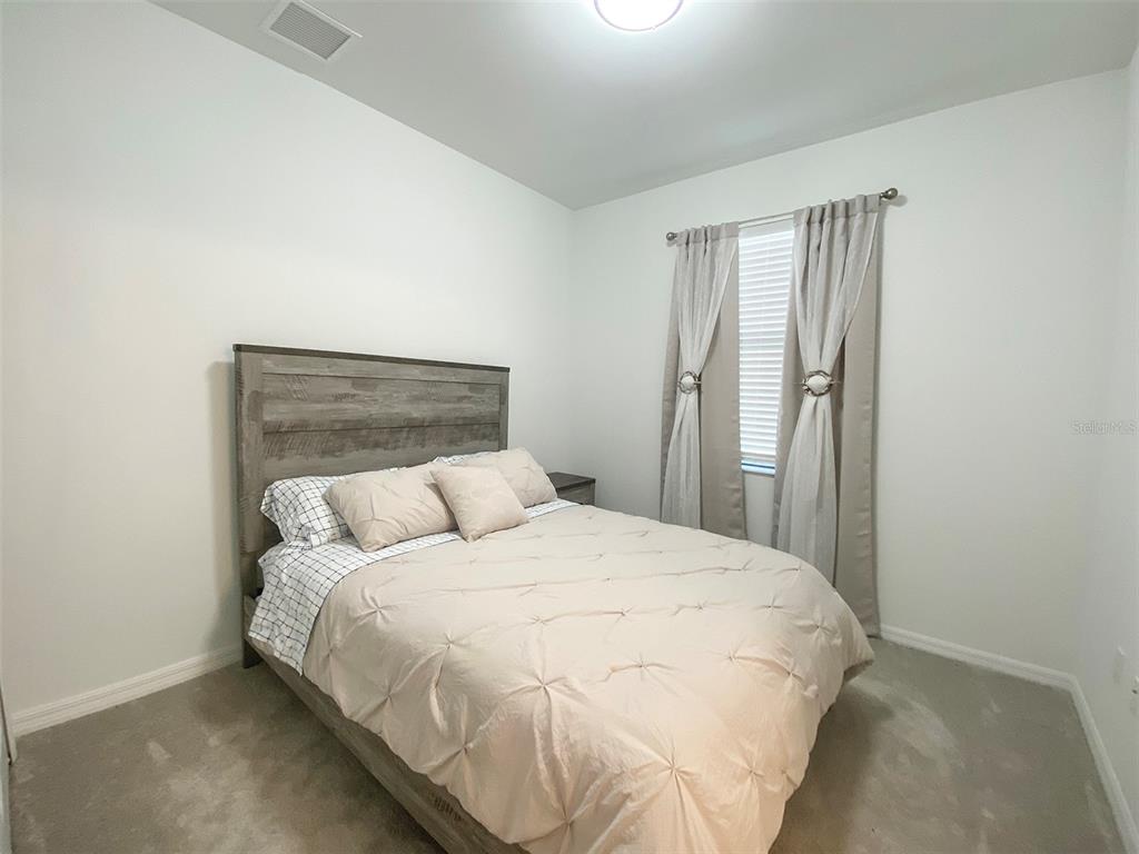 A bedroom features a wooden bed frame, a beige tufted comforter, and light-colored curtains — 15936 HONEYSUCKLE STREET, PORT CHARLOTTE, FL