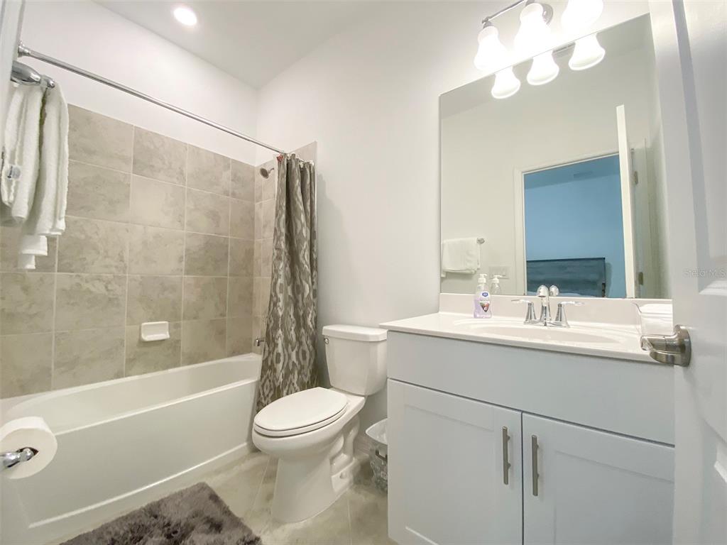 A bathroom features a white vanity, a toilet, and a bathtub with a tiled surround — 15936 HONEYSUCKLE STREET, PORT CHARLOTTE, FL
