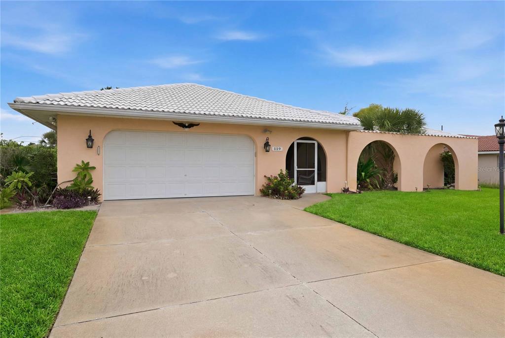 A single-story peach-colored house features a two-car garage, arched entryway, and a concrete driveway — 119 VAN DYCK DRIVE, NOKOMIS, FL