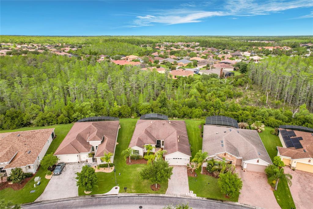 An aerial view shows three suburban houses with screened-in pools backing onto a dense forest — 477 VILLA PARK ROAD, POINCIANA, FL