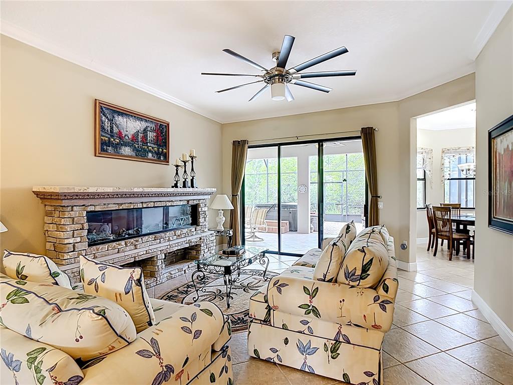 A living room features a stone fireplace, floral sofas, tile flooring, and a sliding glass door — 477 VILLA PARK ROAD, POINCIANA, FL