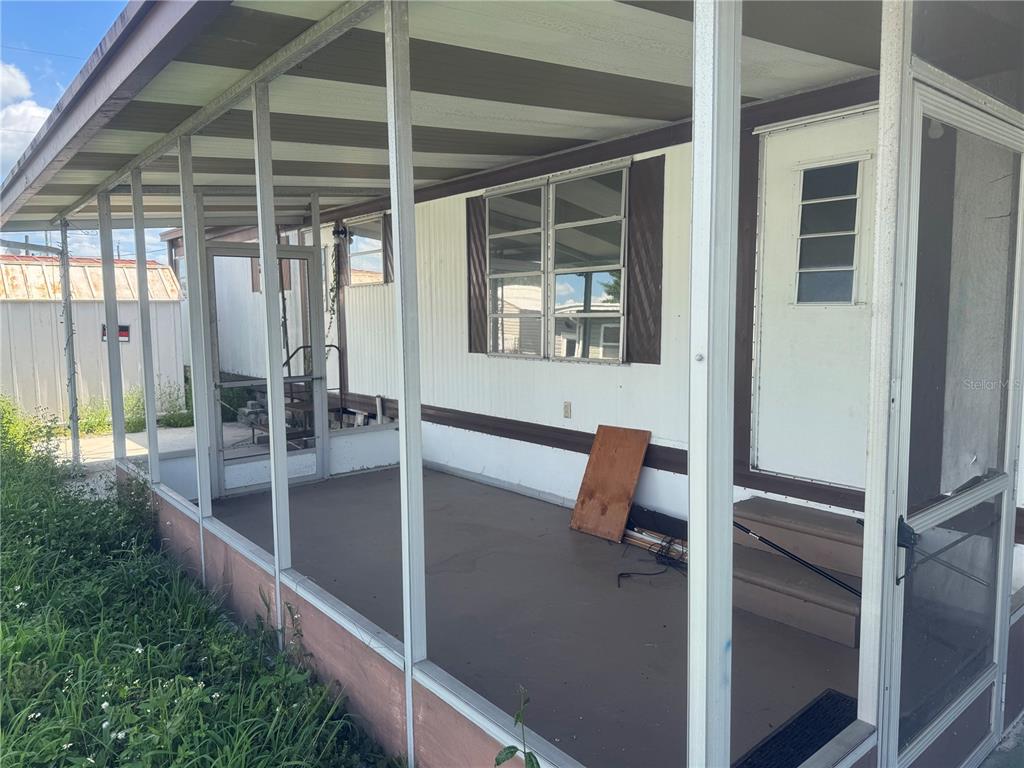 A screened-in porch with a concrete floor, white siding, and a single entry door — 37309 8TH AVENUE UNIT 161, ZEPHYRHILLS, FL