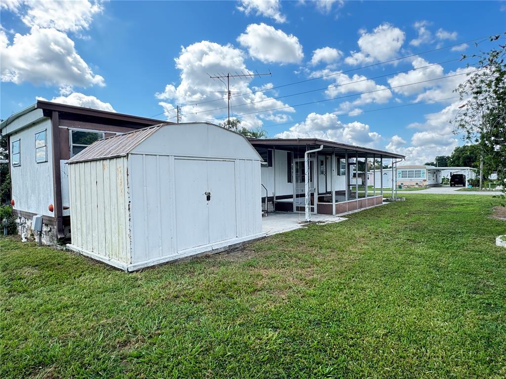 A white metal shed stands in the grass next to a mobile home with a porch — 37309 8TH AVENUE UNIT 161, ZEPHYRHILLS, FL