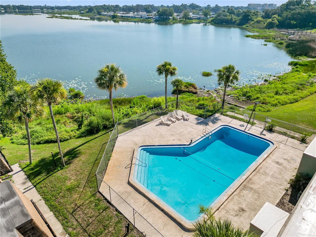 An elevated view of a swimming pool enclosed by a fence next to a lake — 1836 N CRYSTAL LAKE DRIVE UNIT 27, LAKELAND, FL