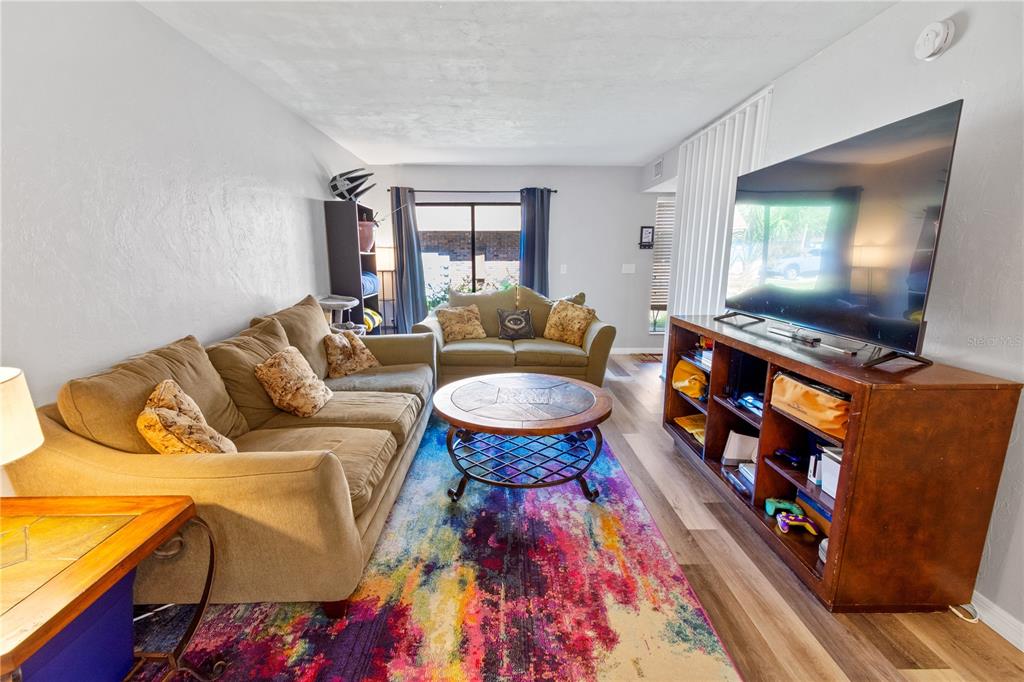 A living room features a tan sofa, a colorful area rug, and a large television — 1836 N CRYSTAL LAKE DRIVE UNIT 27, LAKELAND, FL
