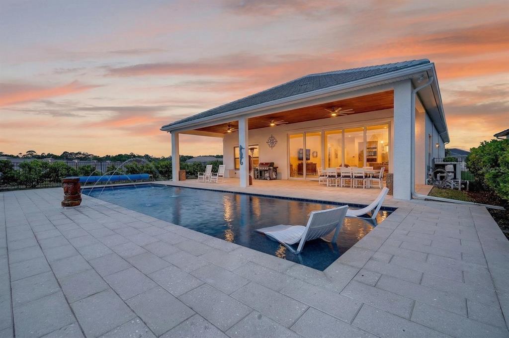A backyard swimming pool with lounge chairs sits before a covered patio at sunset — 94 DEL PALMA DRIVE, PALM COAST, FL