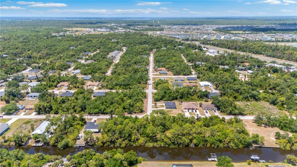 An aerial view shows a residential neighborhood with houses, dense trees, and a canal — 2042 COMO STREET, PORT CHARLOTTE, FL