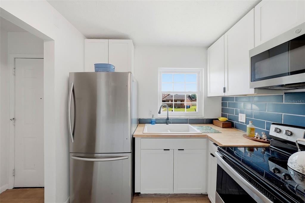 A kitchen features white cabinets, stainless steel appliances, a wood countertop, and blue subway tile — 10310 BLUE FIELD CT, THONOTOSASSA, FL