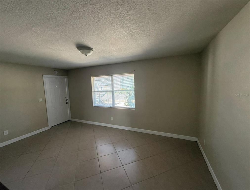 An empty room features beige walls, a white door, a window, and tiled flooring — 117 N EVERGREEN AVENUE UNIT 102, CLEARWATER, FL