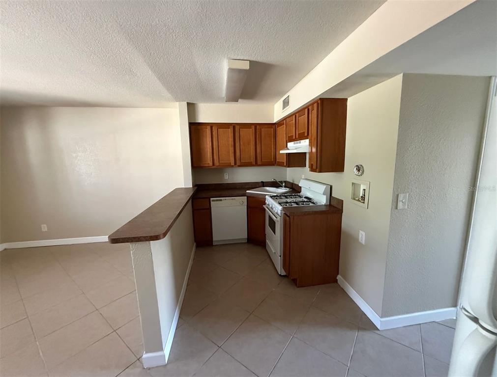 A kitchen with wood cabinets, white appliances, and a breakfast bar overlooking a tiled area — 117 N EVERGREEN AVENUE UNIT 102, CLEARWATER, FL