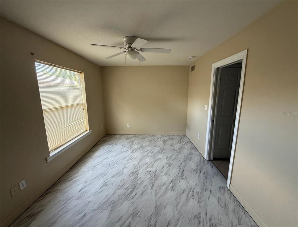 An empty bedroom features light-colored walls, a ceiling fan, and marble-patterned flooring — 117 N EVERGREEN AVENUE UNIT 102, CLEARWATER, FL