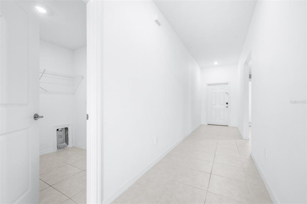 A bright hallway with light tile flooring leads to a white door and laundry closet — 4312 FABULOUS FINCH LANE, BARTOW, FL