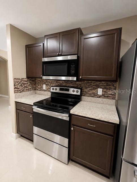 A kitchen features dark wood cabinets, stainless steel appliances, and a tiled backsplash — 171 SHADOWVIEW COURT, LEHIGH ACRES, FL