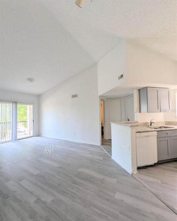 A living room with vaulted ceilings and light wood flooring opens to a kitchen area — 1956 LAKE ATRIUMS CIRCLE UNIT 144, ORLANDO, FL