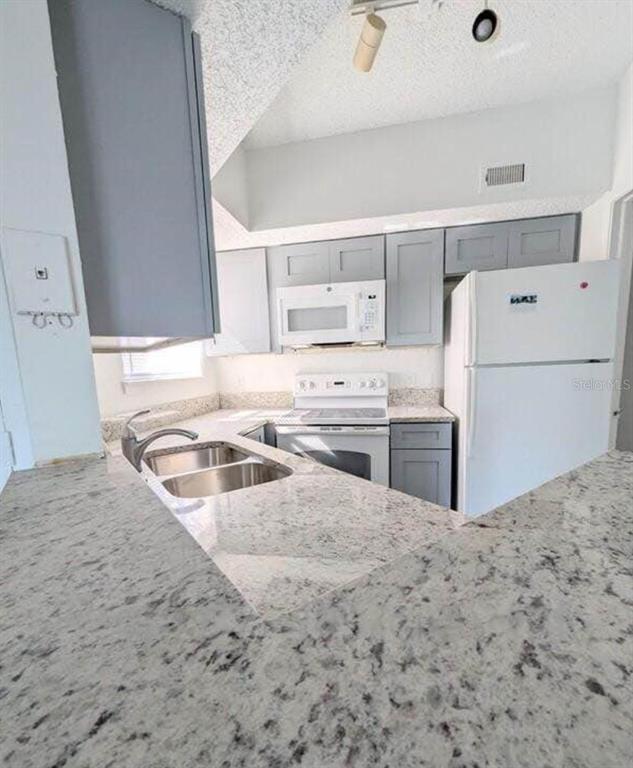 A kitchen features gray cabinets, granite countertops, a double sink, and white appliances — 1956 LAKE ATRIUMS CIRCLE UNIT 144, ORLANDO, FL