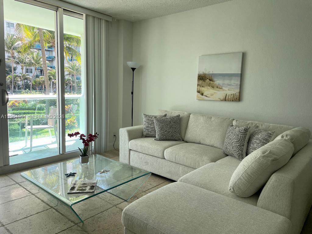 A living room features a beige sectional sofa, a glass coffee table, and a balcony view — 3901 S Ocean Dr # 1J, Hollywood FL 33019, HOLLYWOOD, FL