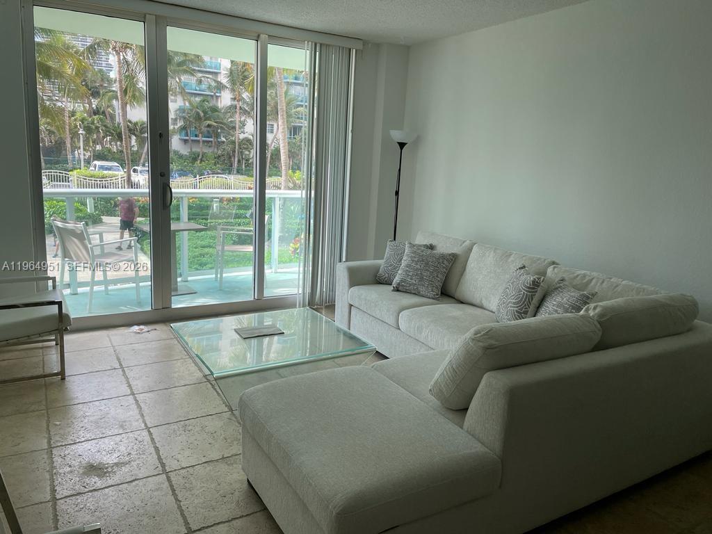 A living room features a light-colored sectional sofa, a glass coffee table, and balcony access — 3901 S Ocean Dr # 1J, Hollywood FL 33019, HOLLYWOOD, FL