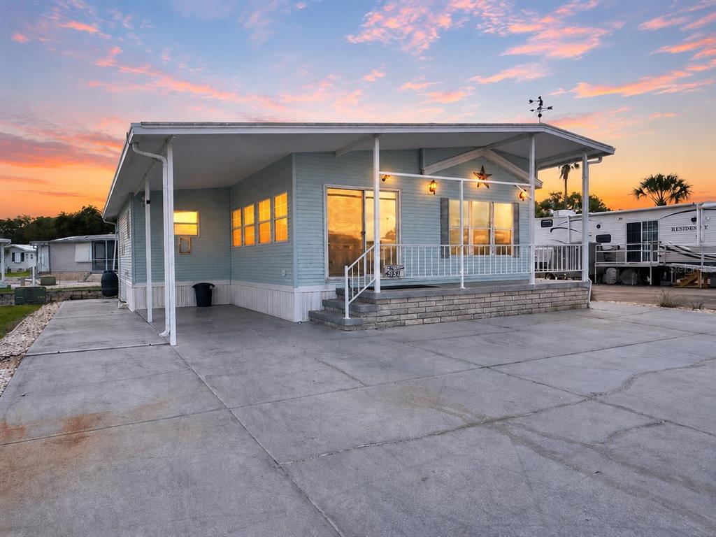 A light blue manufactured home with a concrete driveway, covered porch, and brick skirting — 35151 DANNY DRIVE Lot 114, ZEPHYRHILLS, FL